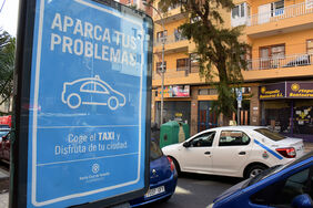 Un taxi pasa junto al soporte publicitario de la campaña que promueve el uso del transporte público en esta Navidad en la calle Ramón y Cajal.